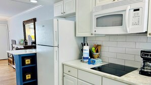 Una cocina con armarios blancos, un refrigerador blanco, un microondas, una cafetera y un lavabo.