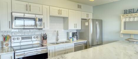 A kitchen with white cabinets, stainless steel appliances, and a marble countertop.