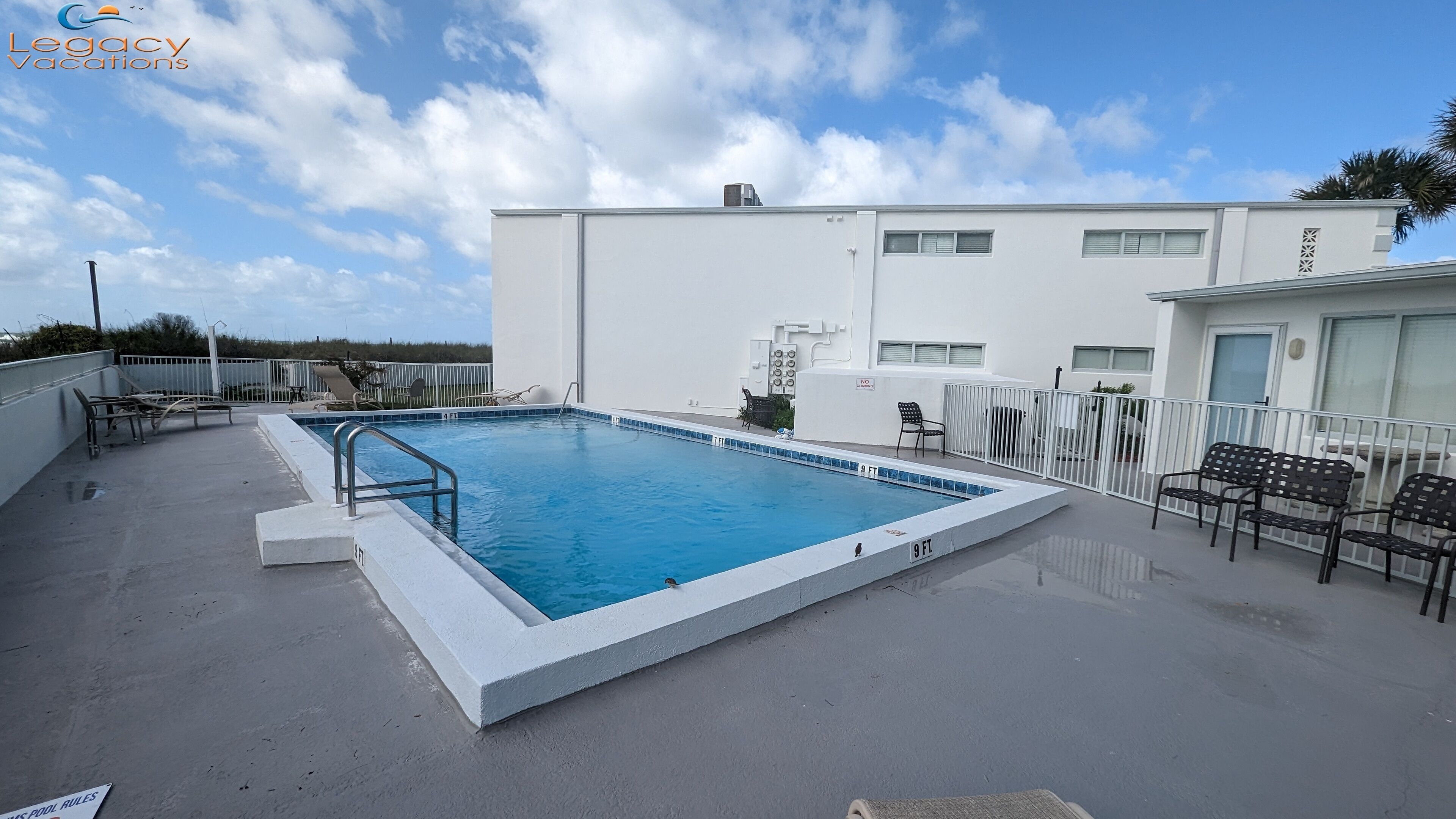 A rooftop pool with a clear blue sky, white walls, and a few lounge chairs.