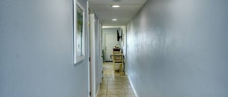A narrow hallway with light blue walls, a tiled floor, and a wooden chair in the distance.