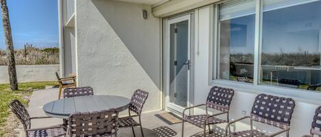 A patio with a round table and six wicker chairs, a sliding glass door, and a view of the beach.