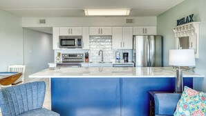 Una cucina moderna con mobili bianchi, un'isola in marmo, elettrodomestici in acciaio inossidabile e una parete decorata in blu.