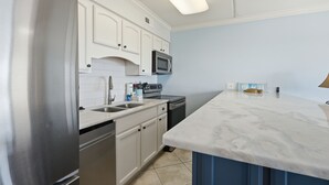 A kitchen with white cabinets, a stainless steel refrigerator, a microwave, and a dishwasher.