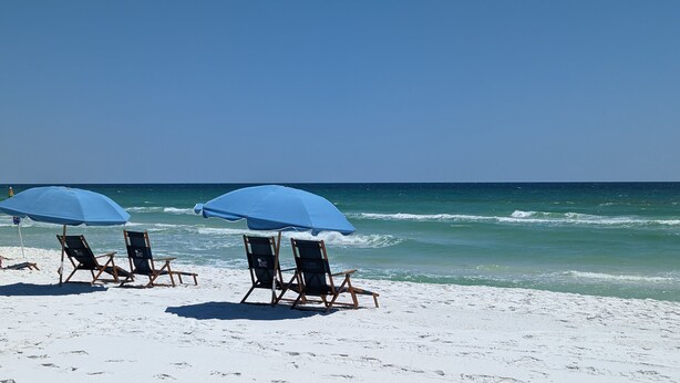 A beach with three beach chairs and two blue umbrellas.