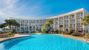 Um hotel com uma piscina grande, várias varandas e palmeiras.