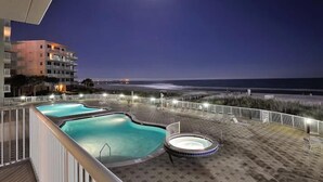 A rooftop pool area with a view of the beach and ocean at night.