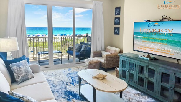 A spacious living room with a large TV, comfortable seating, and a view of the ocean.