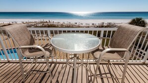 Eine Terrasse mit zwei Korbstühlen und einem Glastisch, mit Blick auf einen Strand und einen klaren Meerblick.