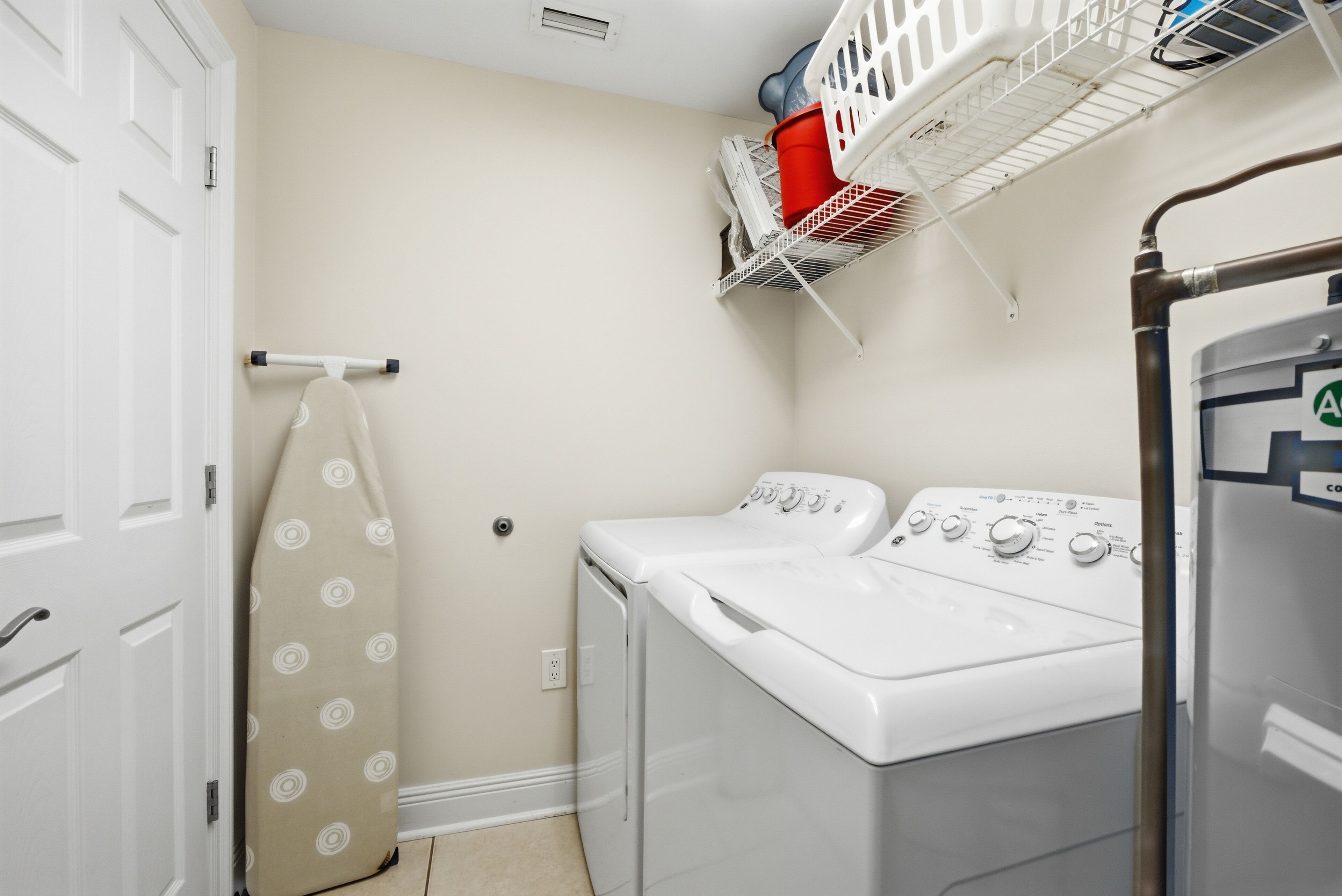 Una sala de bugaderia amb dues rentadores i dues assecadores, un tendal i una porta.