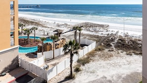 Vista de una playa con una terraza de madera, piscina y un edificio con balcones.