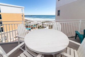 Un balcon avec une table et des chaises blanches, donnant sur une plage et l’océan.