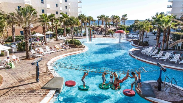 Zona de piscina con sillones de descanso y palmeras, rodeada de edificios.