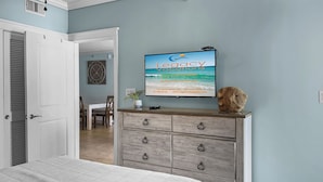 Un dormitorio con cama, cómoda, televisor mostrando 'Legacy vacations' y puerta que da a otra habitación.
