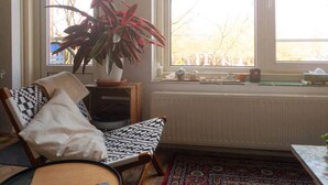 Een knus vertrek met een gestreept stoel, een klein rond tafeltje, een potplant en uitzicht buiten door een raam.