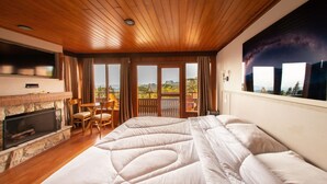 A bedroom with a large bed, a fireplace, a TV, and a balcony with a scenic view. - Surya Pan Hotel e Eventos (Campos do Jordão)