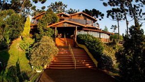 A wooden staircase leading to a multi-level house surrounded by lush greenery. - Surya Pan Hotel e Eventos (Campos do Jordão)