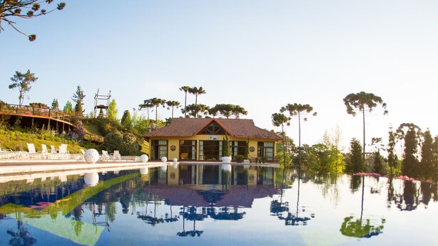 A hotel with a swimming pool, a patio with lounge chairs, and a view of the surrounding landscape. - Surya Pan Hotel e Eventos (Campos do Jordão)