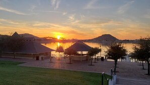 A lakeside view with a sunset, a gazebo, and a building with a sloped roof. - 5 STAR Goodyear Spring Training Hiking Mountain Views Heated Pool Included (Goodyear)