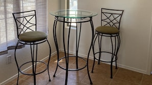 A dining area with two chairs, a glass table, a chandelier, and decorative wall art. - 5 STAR Goodyear Spring Training Hiking Mountain Views Heated Pool Included (Goodyear)