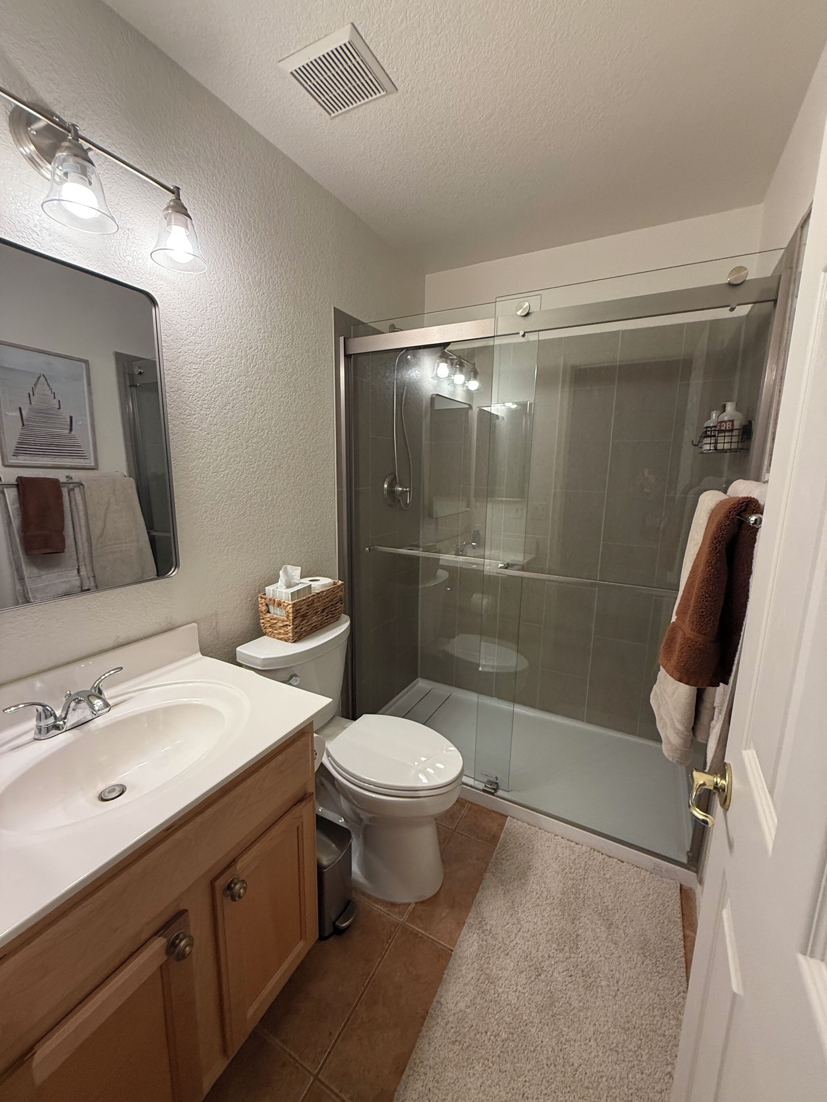 A bathroom with a glass-enclosed shower, a white sink, and a toilet.