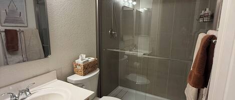 A bathroom with a glass-enclosed shower, a white sink, and a toilet.