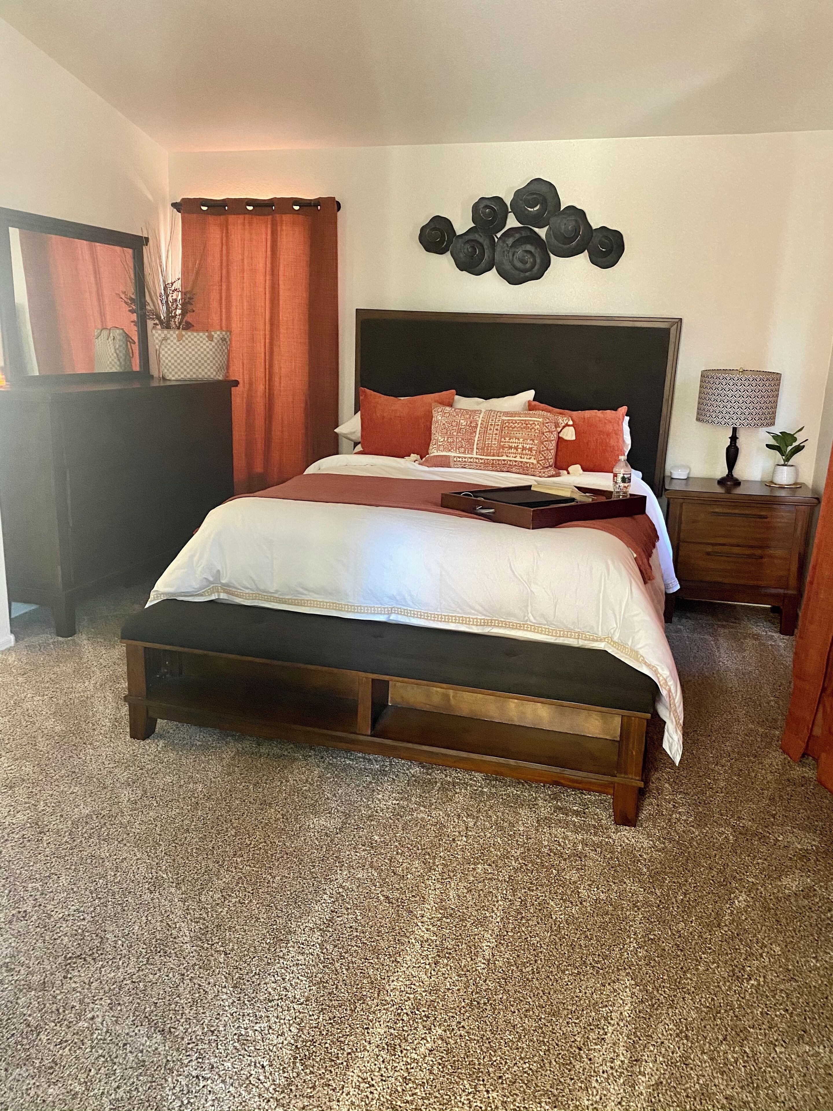 A bedroom with a wooden bed, a headboard, a bedside table with a lamp, and a wall decoration.