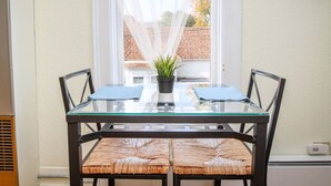 A dining table with a glass top, surrounded by wicker chairs, in a room with a window and a plant on the table. - Palmer House, Studio 4, Cozy Downtown Studio for 2, Local Golfing 50% Off! (Baker City)