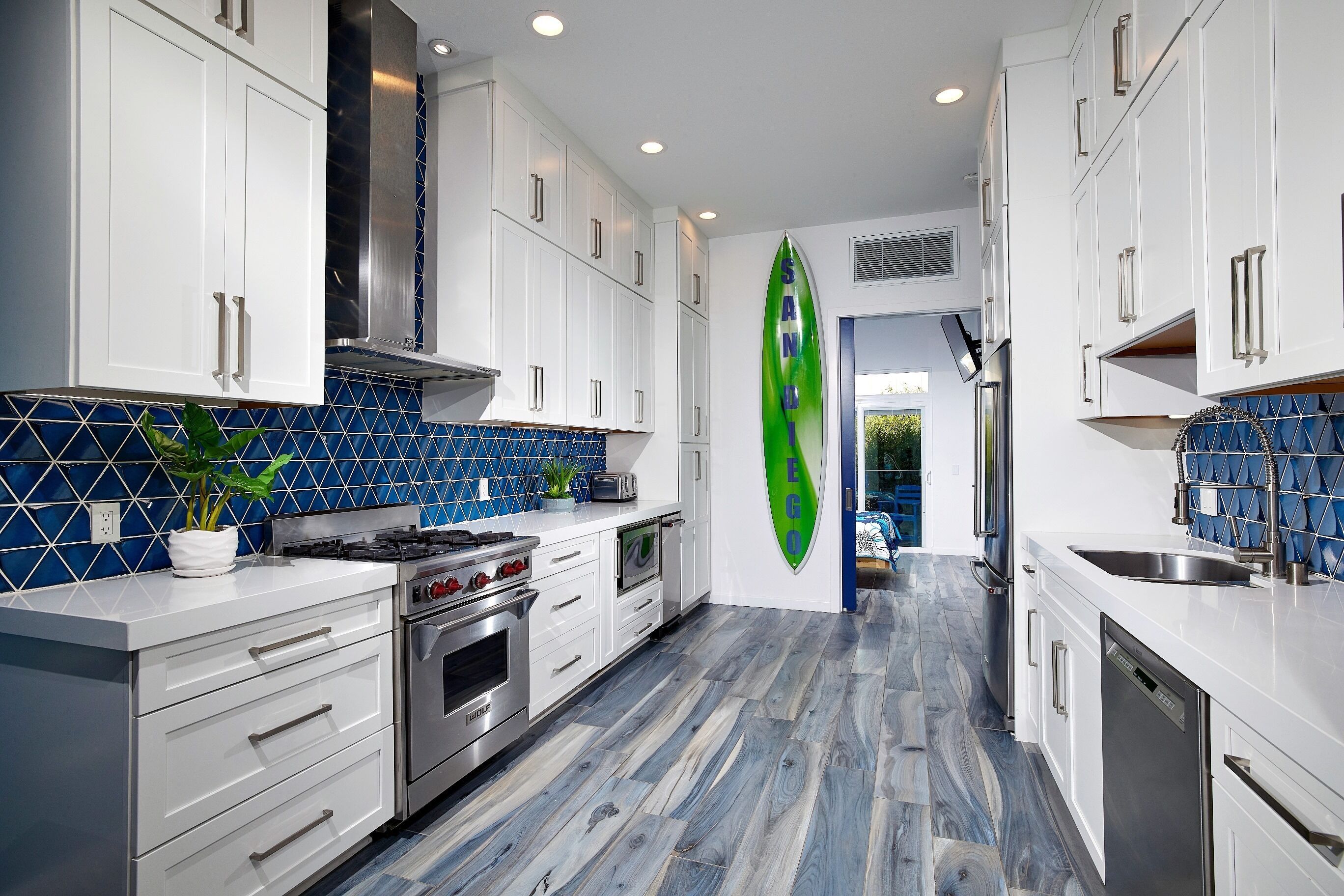 Een moderne keuken met witte kasten, een blauwe betegelde achterwand en een surfboard decoratie.