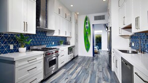 A modern kitchen with white cabinets, a blue-tiled backsplash, and a surfboard decoration.