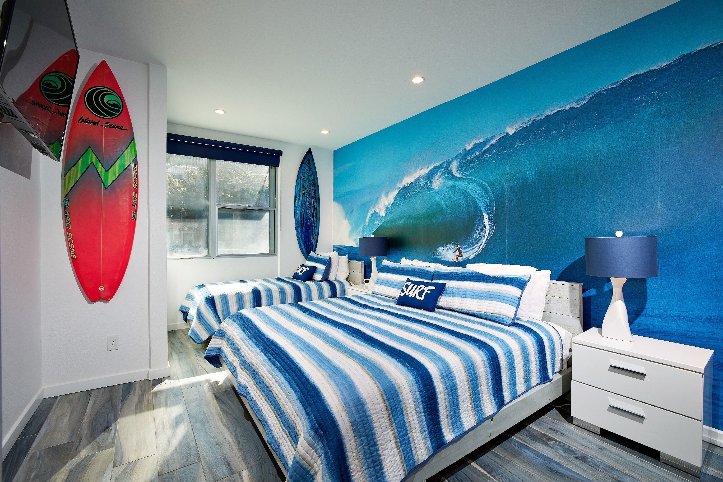 Een slaapkamer met twee bedden, een grote muurschildering van een golf en surfplanken aan de muur.