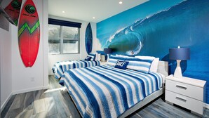 A bedroom with two beds, a large wave mural, and surfboards on the wall.