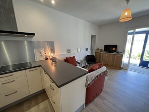 A modern kitchen with a central island, a dining area with a red sofa, and a TV in the background.