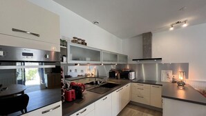 A modern kitchen with stainless steel appliances, white cabinetry, and a central island with a sink.