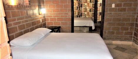 Een kamer met een bed, een klein tafeltje en een bakstenen muur.