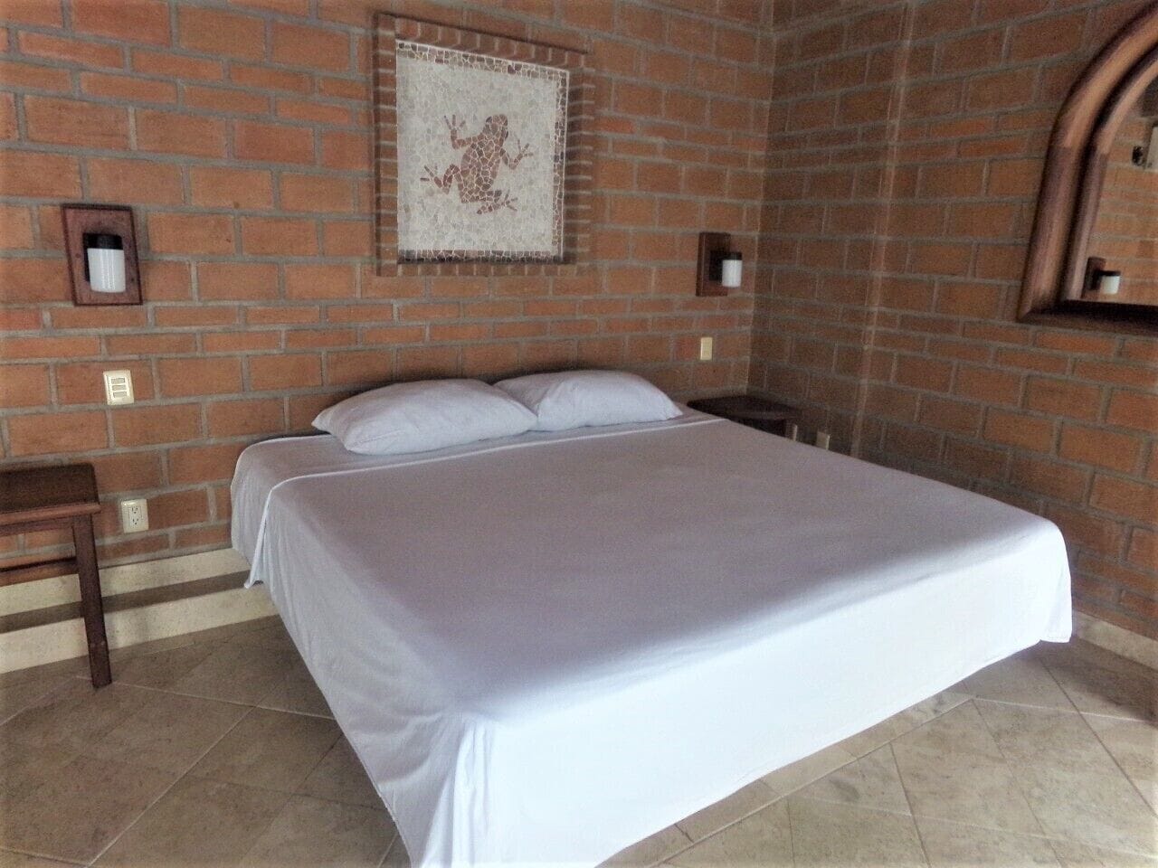 Quarto com cama grande, parede de tijolos e um quadro emoldurado sobre a cama.