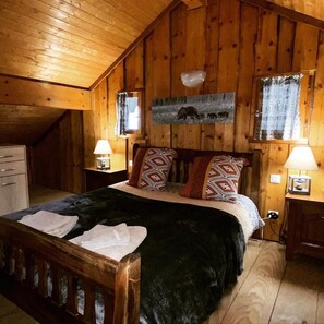 Een gezellig slaapkamer in een houten hut, met een bed, twee nachtkastjes, een dressoir en een raam met gordijnen.
