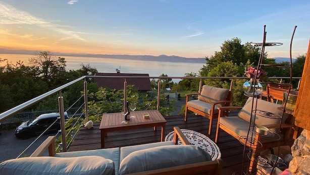 Une terrasse avec des sièges, une table et une vue sur un plan d’eau et des montagnes.