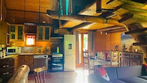 Une cuisine rustique avec des poutres en bois, un coin repas avec une table et des chaises, et un salon avec un canapé.