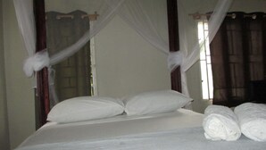 Una cama con sábanas blancas, dosel y toallas enrolladas.