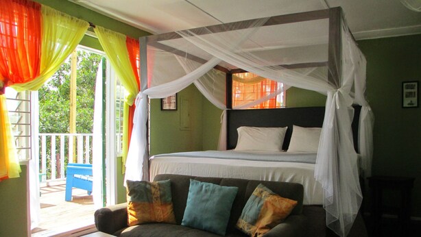 Una habitación con cama con dosel, un sofá con cojines y un balcón con una silla.