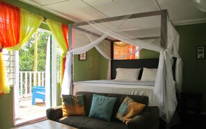A room with a four-poster bed, a sofa with cushions, and a balcony with a chair.