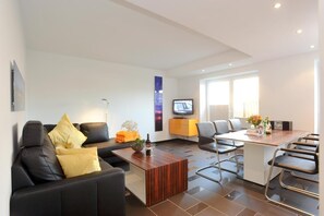 Una sala de estar moderna con un sofá, una mesa de centro y un televisor. Hay un comedor con una mesa y sillas.