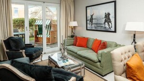 Een woonkamer met een groene bank, zwarte fauteuils en een beige bank. Er is een glazen salontafel, een lamp en een schilderij aan de muur.