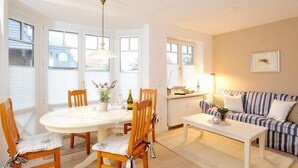 A cozy living room with a dining area, featuring a round table, wooden chairs, a striped sofa, and a radiator. - Alte Stadtgärtnerei, Whg. 11 - Old city nursery (Sylt)