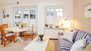 A modern living room with a dining area, a sofa, a coffee table, and a lamp. - Alte Stadtgärtnerei, Whg. 11 - Old city nursery (Sylt)