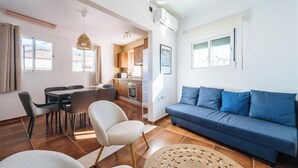 Un salon avec un canapé, une table à manger avec des chaises, et un coin cuisine à l’arrière-plan.
