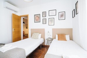 A hotel room with two beds, a wooden door, a small table with a lamp, and several framed pictures on the wall. - Lovely Duplex at Santa Cruz 10 people Parking Optional (Sevilla)