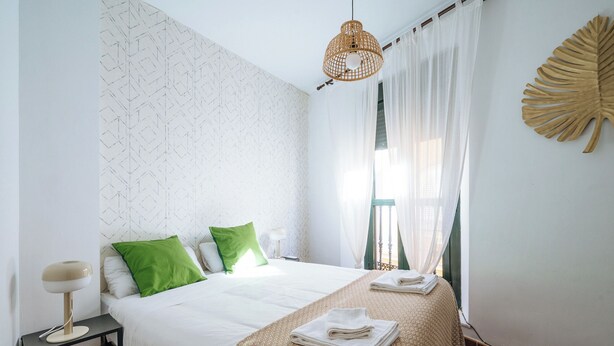 Une chambre à coucher bien rangée, avec un lit, des oreillers, une lampe de chevet et une feuille décorative accrochée au mur.