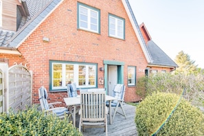 A two-story brick house with a patio area featuring a table and chairs.