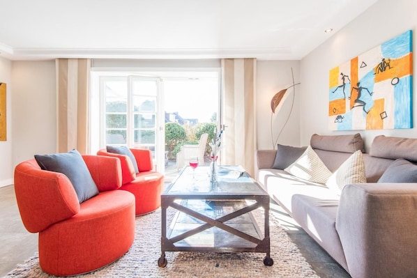 A modern living room with a red sofa, a grey sofa, and a glass coffee table. There is a large window with a view of the outdoors.